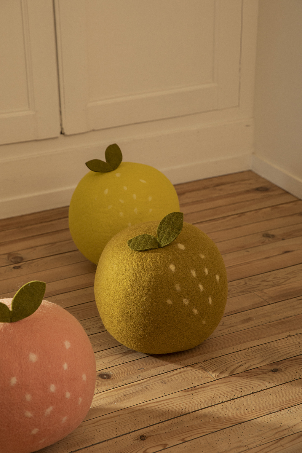 Trio de poufs en feutre de laine en forme de pomme, pêche et citron dans une chambre