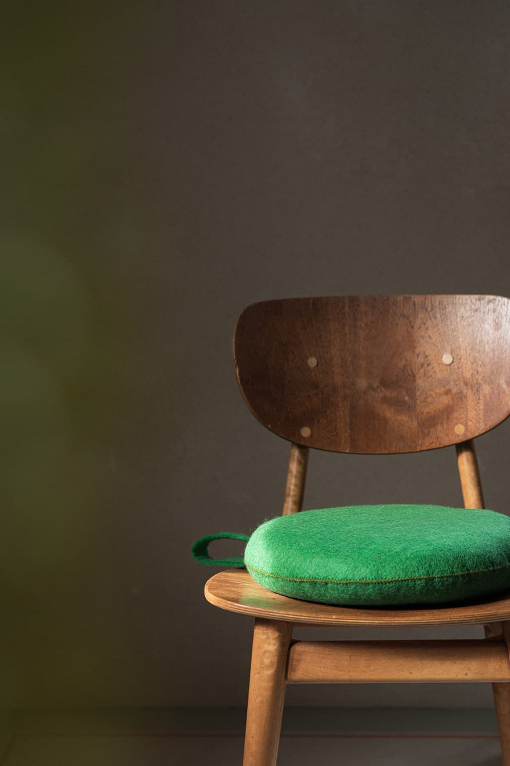 Round green felted wool cushion on a wooden chair