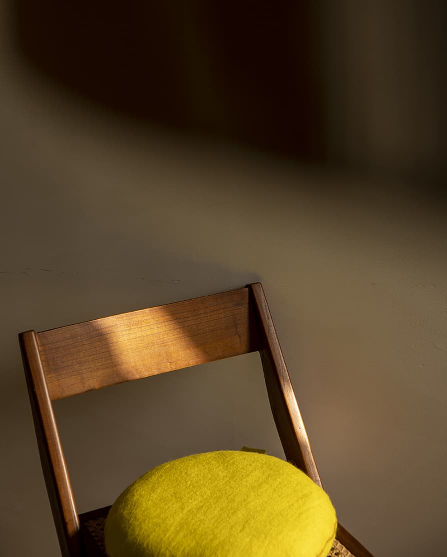 Petit coussin rond jaune en laine feutrée sur une chaise en bois